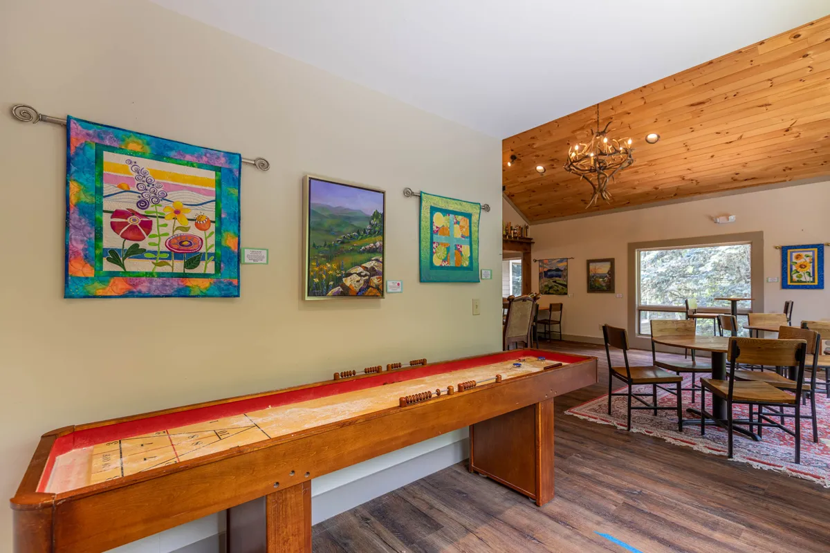 An interior space featuring a game table under colorful wall art, with a view into a dining area. The environment is playful yet homey, inviting guests to gather for board games or cards.