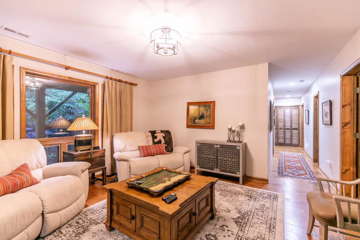 A comfortable living area with ample seating, a wooden coffee table for board games or snacks, and a window with curtains that lets in natural light. The scene is cozy and welcoming, perfect for family game nights or relaxed lounging.