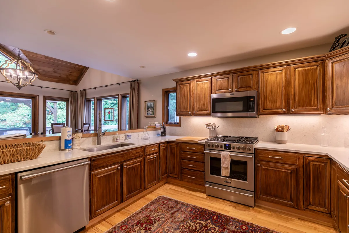 A modern, well-equipped kitchen showcasing stainless steel appliances, generous wooden cabinetry, a central island for meal prep, and large windows letting in ample sunlight. The setup is ideal for cooking and entertaining, with a view that connects the kitchen to the outdoors.