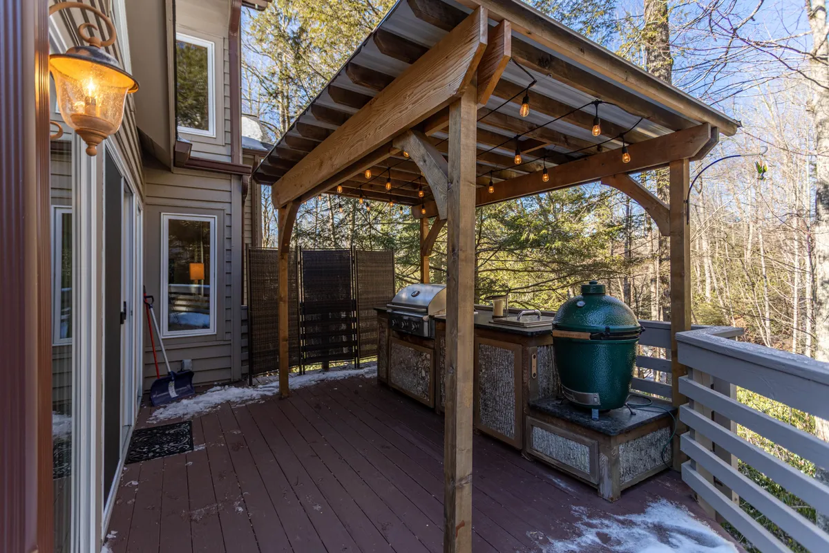 A wooden pergola shelters an outdoor grill and Green Egg smoker, with string lights creating a festive, cozy atmosphere. There’s a dining table for group meals, inviting social gatherings and alfresco feasts as described in the section.