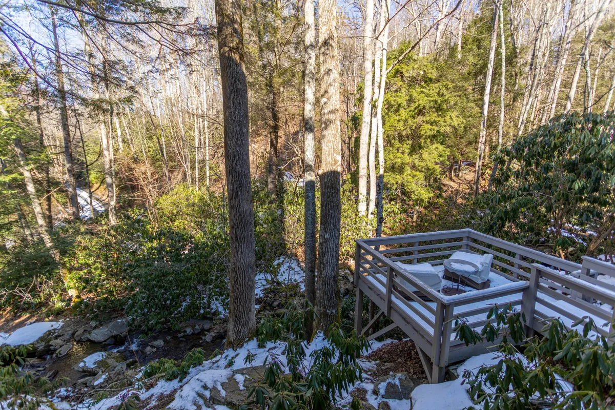 A serene wooden deck nestled among trees, with a view of a gentle stream flowing nearby. The peaceful ambiance makes this spot ideal for relaxing with morning coffee, enjoying sunset views, or watching for wildlife along the water’s edge.