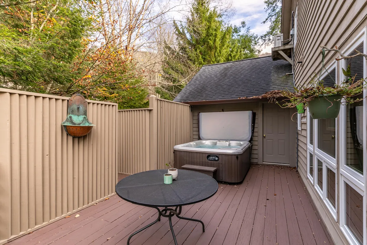 A tranquil outdoor area with a bubbling hot tub, a small round table, and a decorative wall fountain surrounded by trees. The setting is private and cozy, providing an ideal retreat for unwinding after a day of adventure.