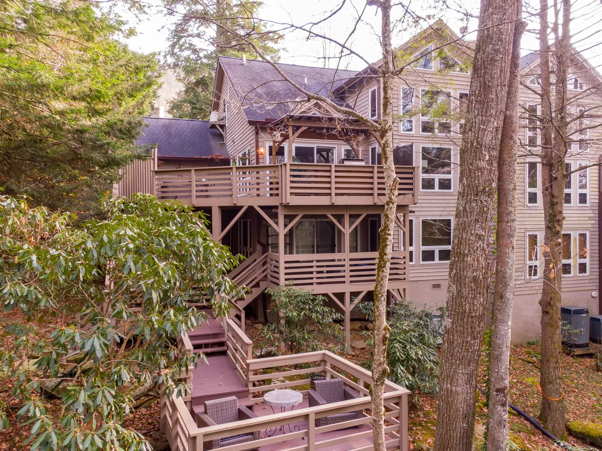 A multi-level deck surrounded by trees, with ample seating and large windows, captures the tranquil outdoor gathering spaces available in all seasons. The deck's vantage point promises sunset views and a seamless blend with nature.