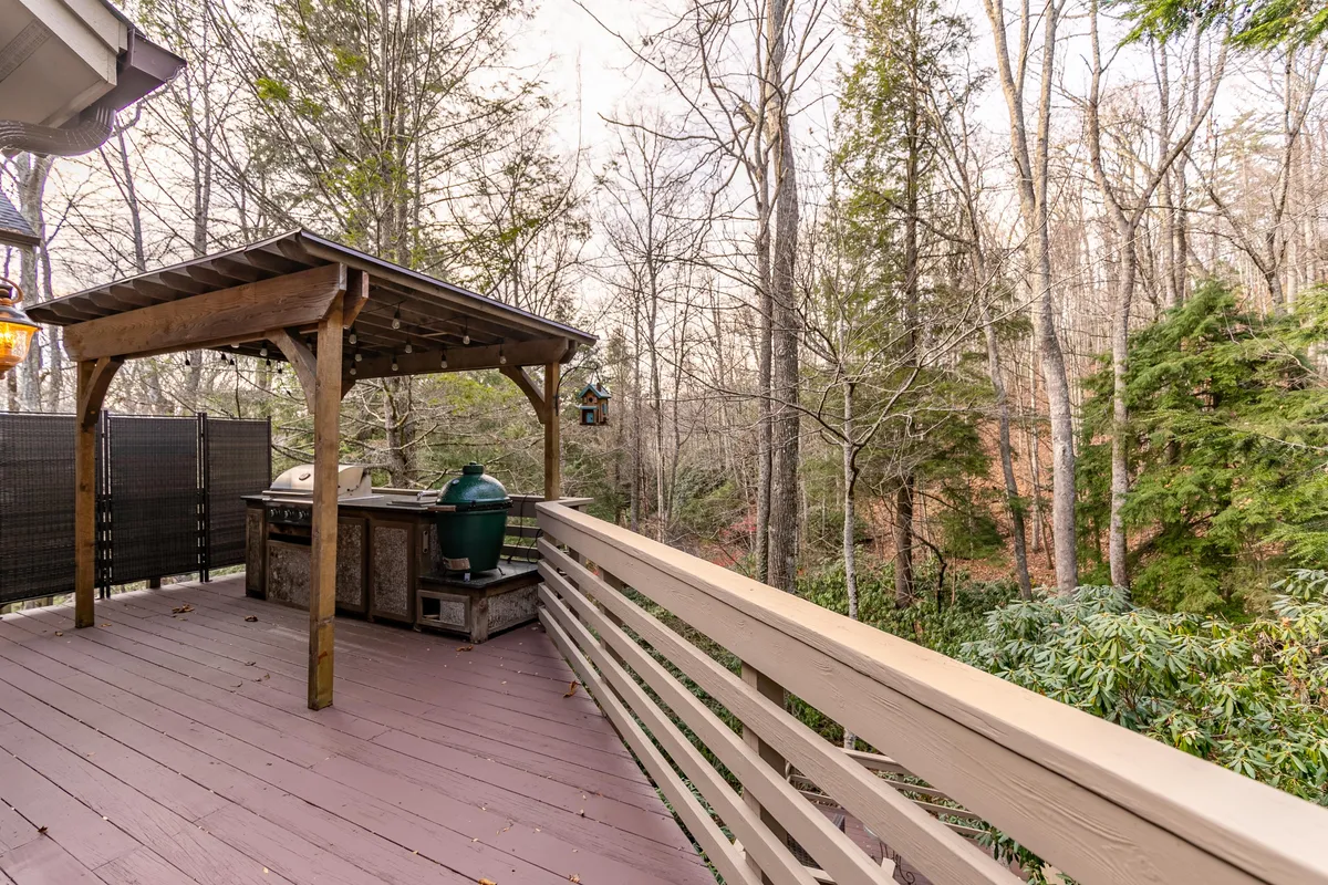 This exterior scene showcases a wooden pergola with an outdoor grill, surrounded by lush greenery. The setup encourages activities like barbecuing, socializing, and enjoying meals outdoors, with a serene background of trees and open sky.